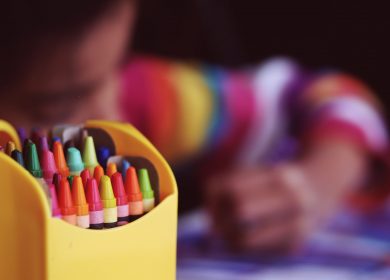 Pack of crayons with a child coloring in the background