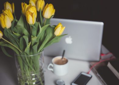 Vase with yellow tulips in it in front of laptop and next to a coffee cup