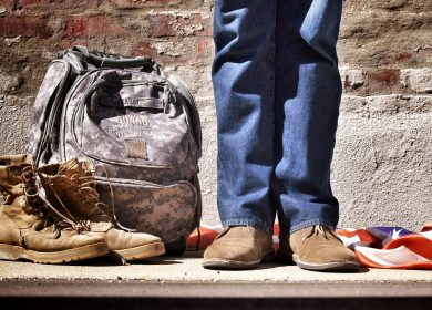 Legs of a person standing next to camoflauged backpack and combat boots