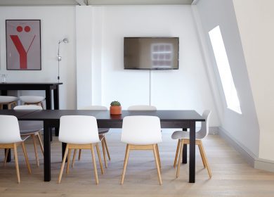 Table with chairs around it with TV on a wall in the background