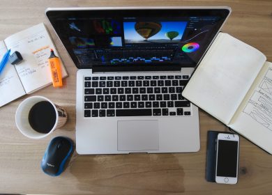 Top view of a laptop open with a cup of coffee, mouse, smartphone and journals open next to it