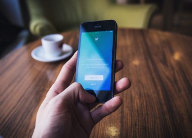 Hand holding smartphone with blue screen over a table with cup and saucer