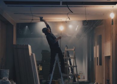 Man on ladder patching the ceiling with drywall boards in the background