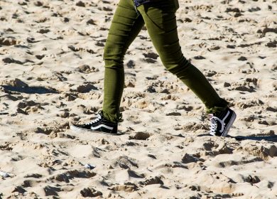 Legs walking on sand with green pants and black shoes on