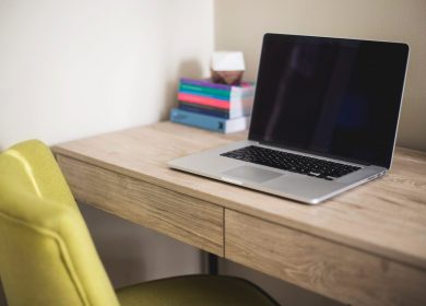 Desk with laptop on it and notepad in the background with a chartruese chair in front of it