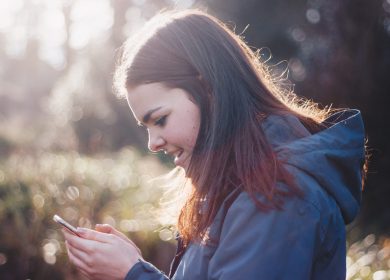View of woman in blue hoodie from left side as she looks at a phone
