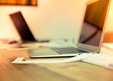 Two laptops on a table with papers around them