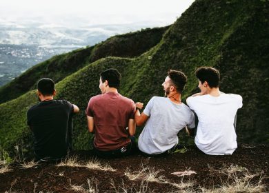 Four men sitting facing green hills