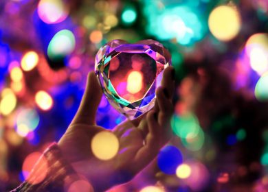 Hand holding up ornament with colorful lights in the background