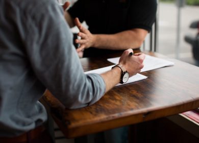 Two people sitting at a desk with paper on it.