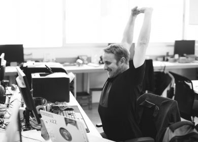 Man at desk with computer and printer stretching with arms in the air
