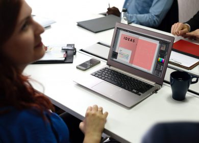 Lady at a desk with a laptop looking up at someone next to her