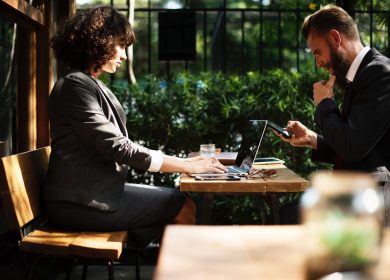 Woman with a laptop sitting across a table from a man with a phone in hand
