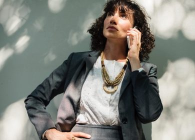 Woman in a business suit with a gold necklace with her hand on her hip and a phone to her ear