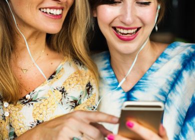 Two women loooking at a smart phone sharing earbuds