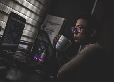 Man looking at laptop computer screen while holding a coffee cup close to his mouth