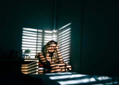 Woman in corner of room with shadow of blinds over her